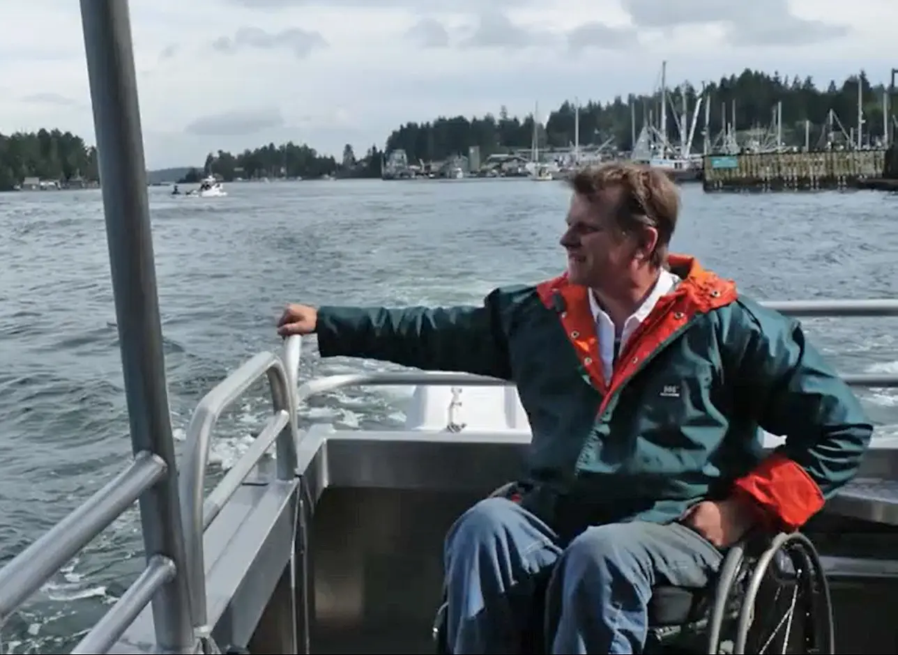 Man in a wheelchair riding on a boat near a marina.