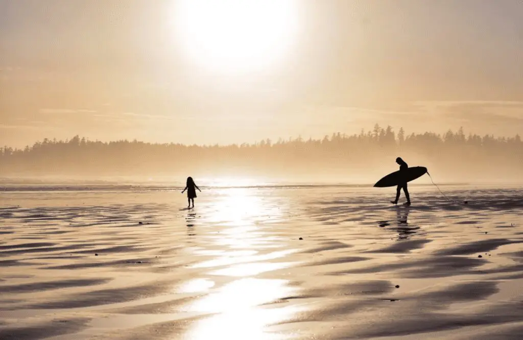 Silhouette of a surfer and a child on a beach at sunset.
